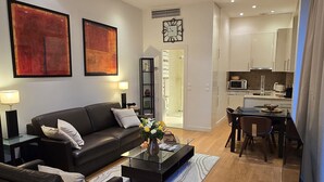 Ein modernes Wohnzimmer mit einer schwarzen Couch, einem Glastisch und einem Essbereich mit Tisch und Stühlen.
