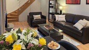 Ein modernes Wohnzimmer mit Treppe, einer schwarzen Ledersofa, einem Couchtisch und einer Blumenvase.