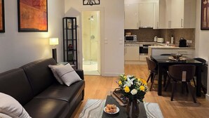 Una sala de estar moderna con un sofá negro, una mesa de centro con un jarrón de flores y una cocina al fondo.