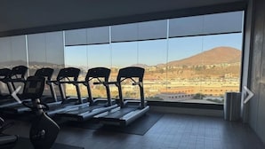 A gym with treadmills and exercise bikes, large windows with a cityscape view. -  Luxury studio w/ rooftop infinity pool & TJ sunset views Cosmopolitan tower!…. (Tijuana)