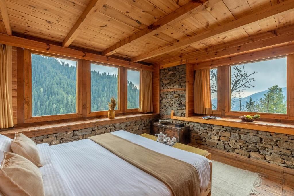 Une chambre située dans une cabane en bois, avec un mur en pierre et de grandes fenêtres donnant sur une forêt.