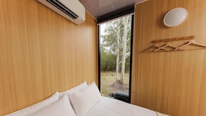 A bedroom with a bed, white pillows, a wooden wall, a window, and a hanging light fixture.