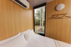 Un dormitorio con cama, almohadas blancas, pared de madera, ventana y lámpara colgante.