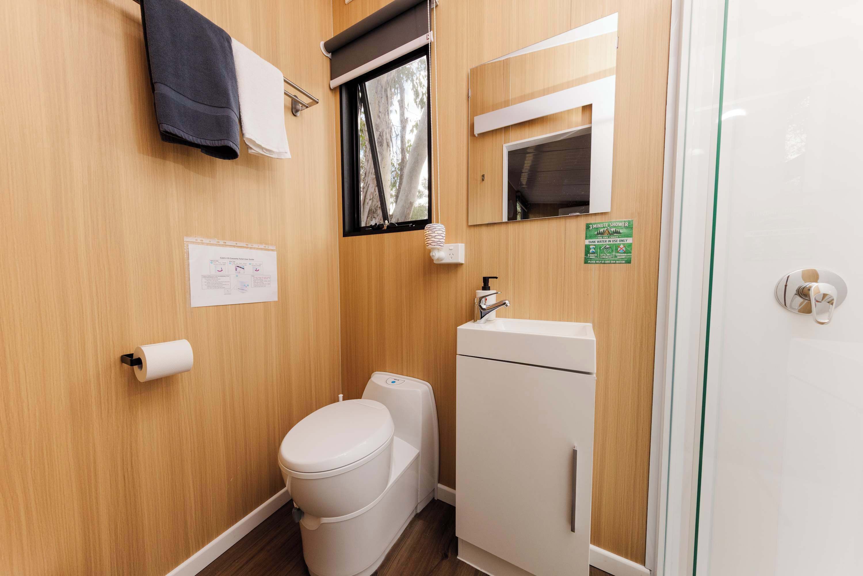 A compact bathroom with a toilet, a sink, a mirror, and a shower area.