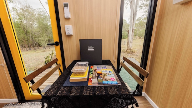 A wooden table with a black lace tablecloth, two wooden chairs, a bench, a book, a magazine, and a small plant.