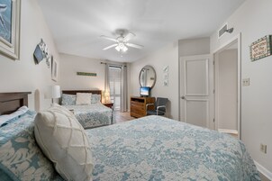 A bedroom with two beds, a ceiling fan, a dresser, a chair, and a television.