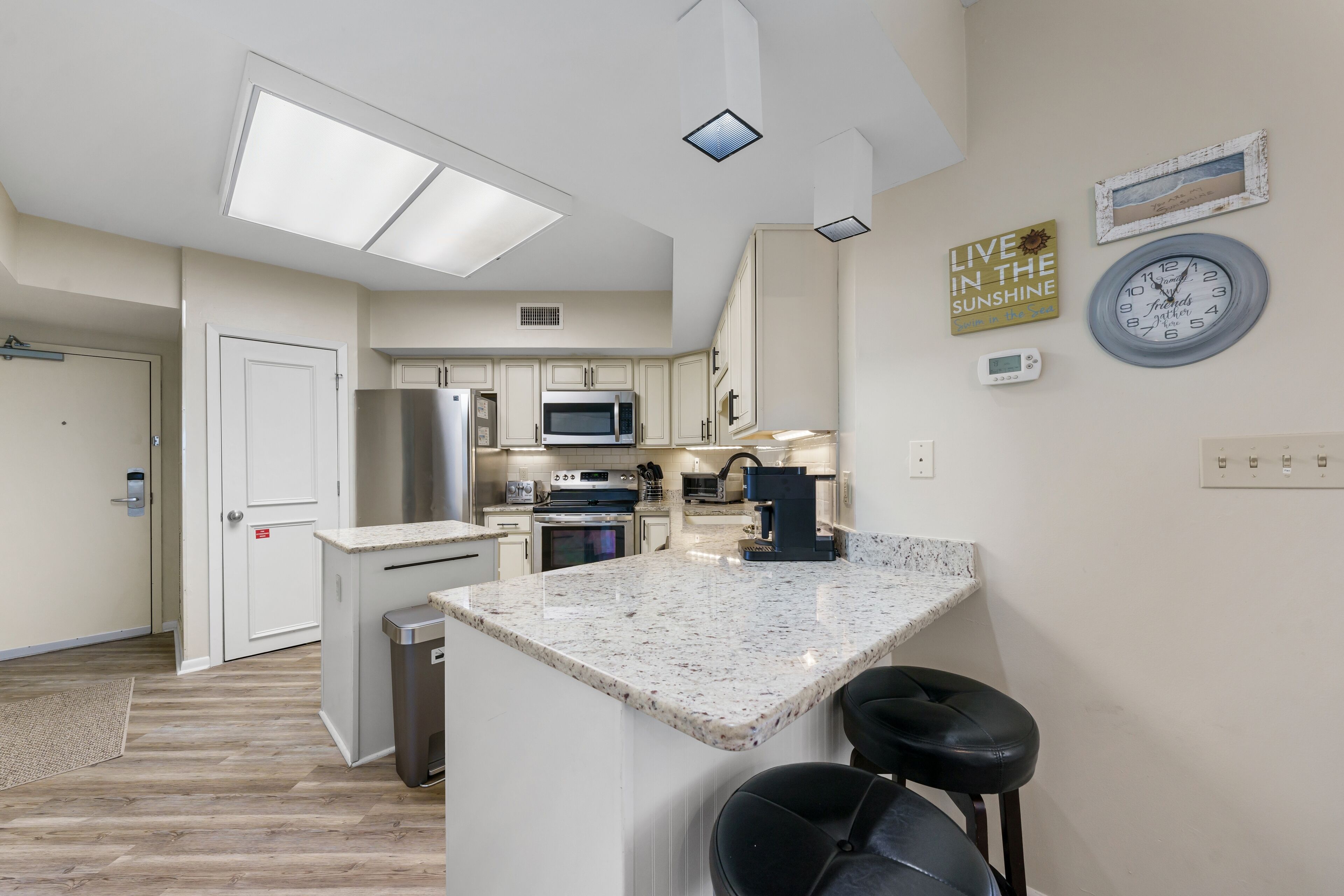 Una cocina moderna con una isla central, electrodomésticos de acero inoxidable y un reloj en la pared.