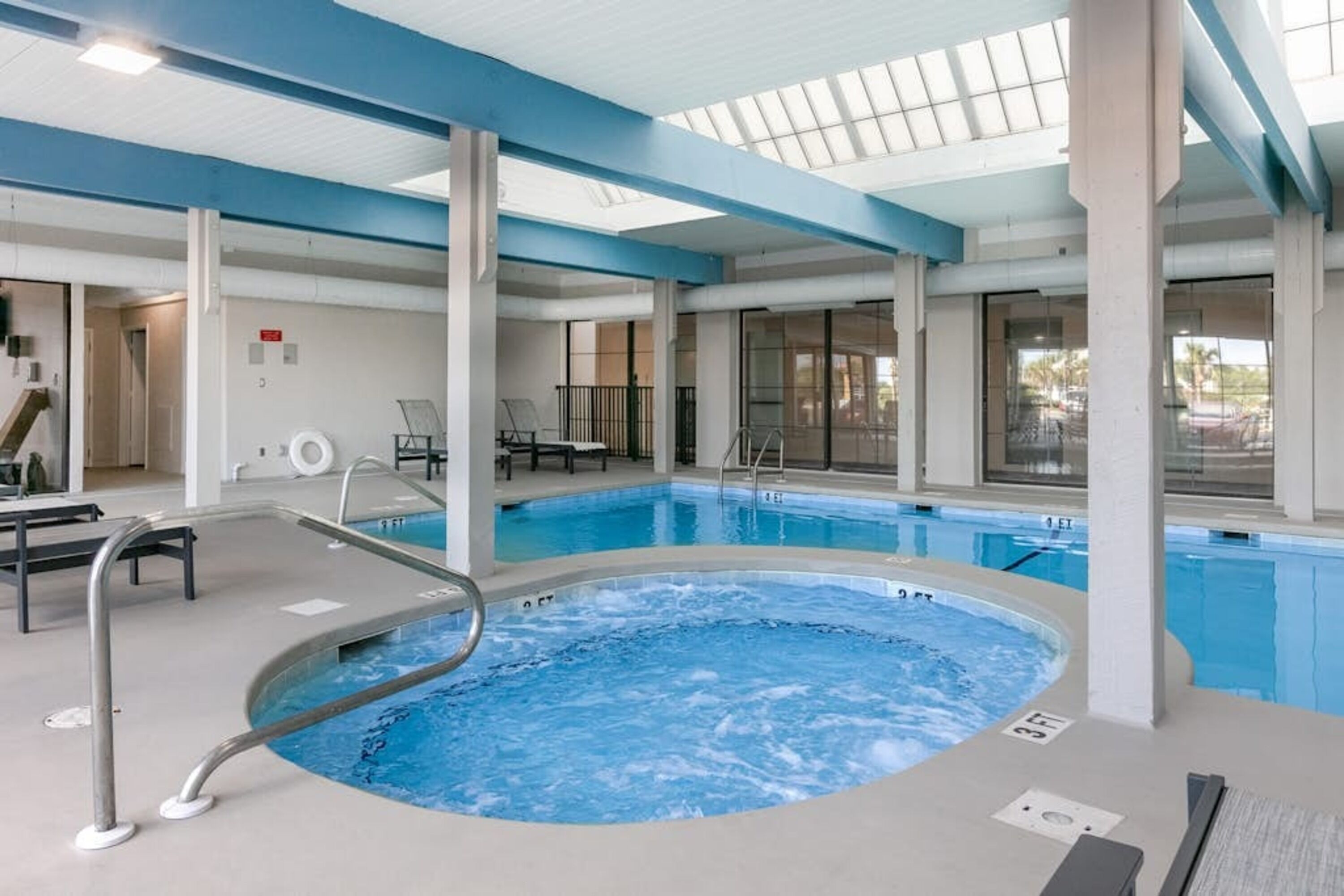 Una piscina interior con jacuzzi, sillas de descanso y un área acristalada con vistas.