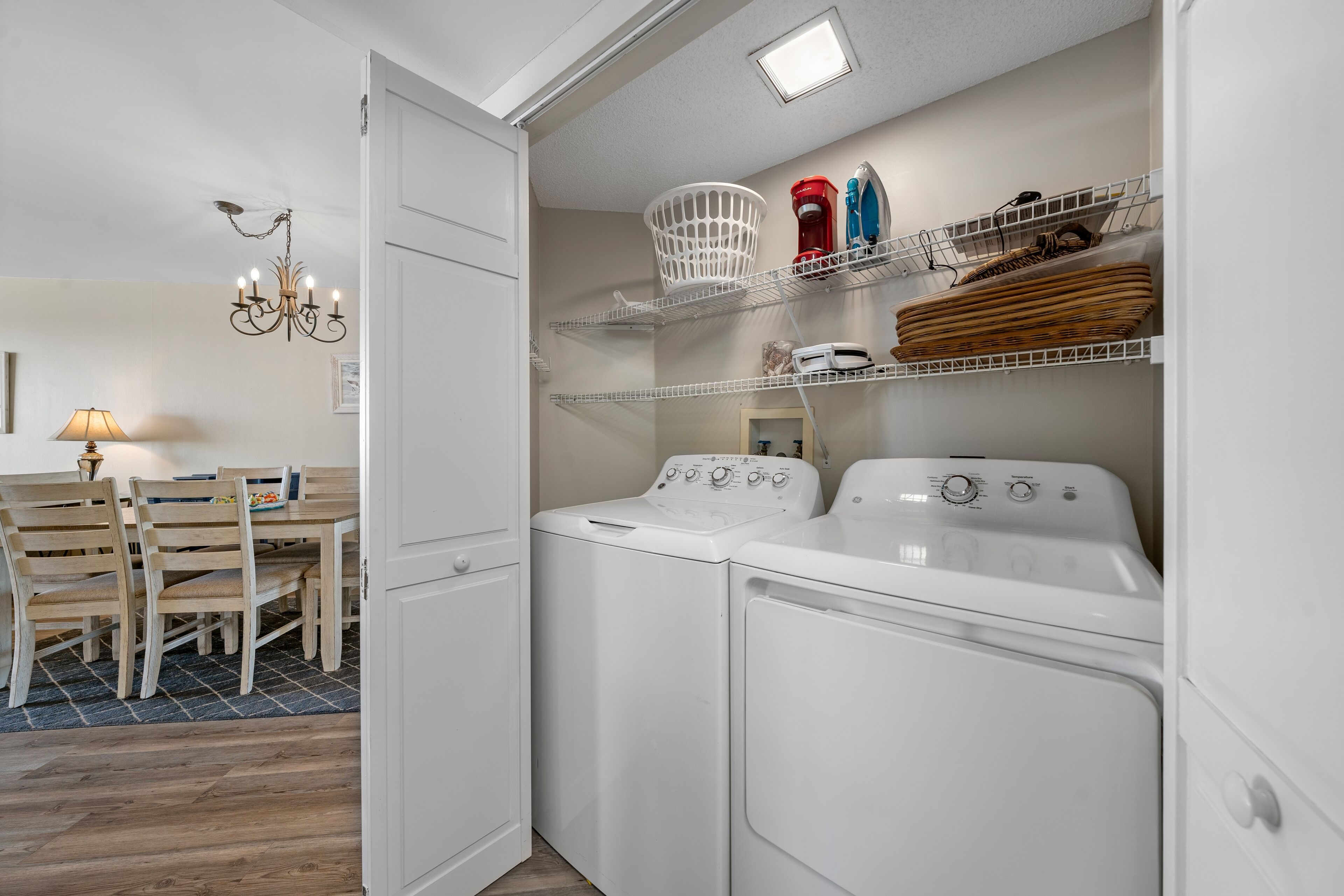 A laundry room with two white washing machines, a basket, and shelves with various items.