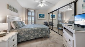 A bedroom with a bed, a TV, a dresser, a mirror, and a ceiling fan. - Bluewater 902 (Orange Beach)