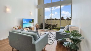 A modern living room with a large TV, grey sofas, a coffee table, and a view of the beach through large windows. - Stylish Apartment Near Mandurah’s Best Spots (Mandurah)