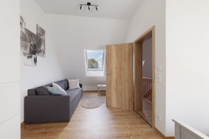 A modern interior with a grey sofa, wooden flooring, a small rug, and a wooden wardrobe.