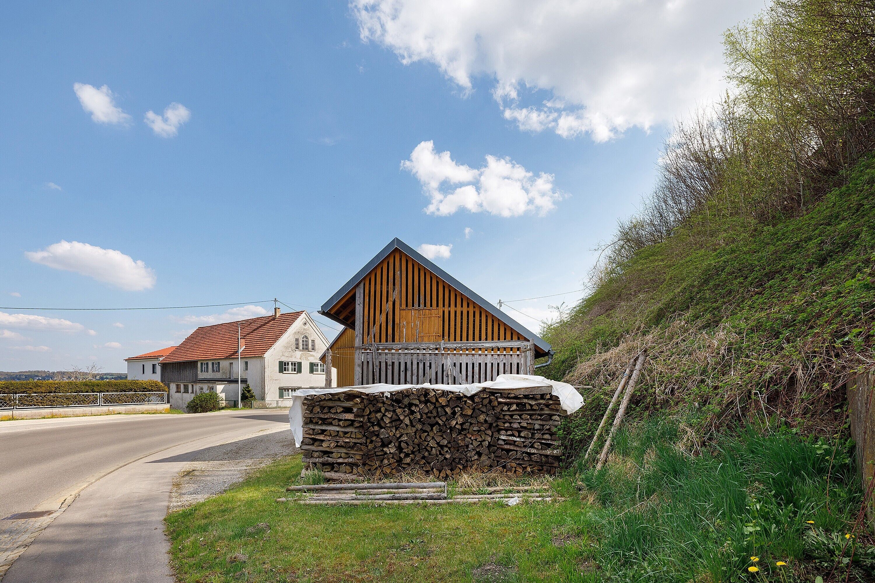 Ein ländliches Haus mit einem geneigten Dach, einem Holzzaun und einem Holzstapel.