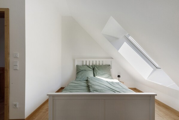 A bedroom with a sloped ceiling, a skylight, and a bed with green bedding.