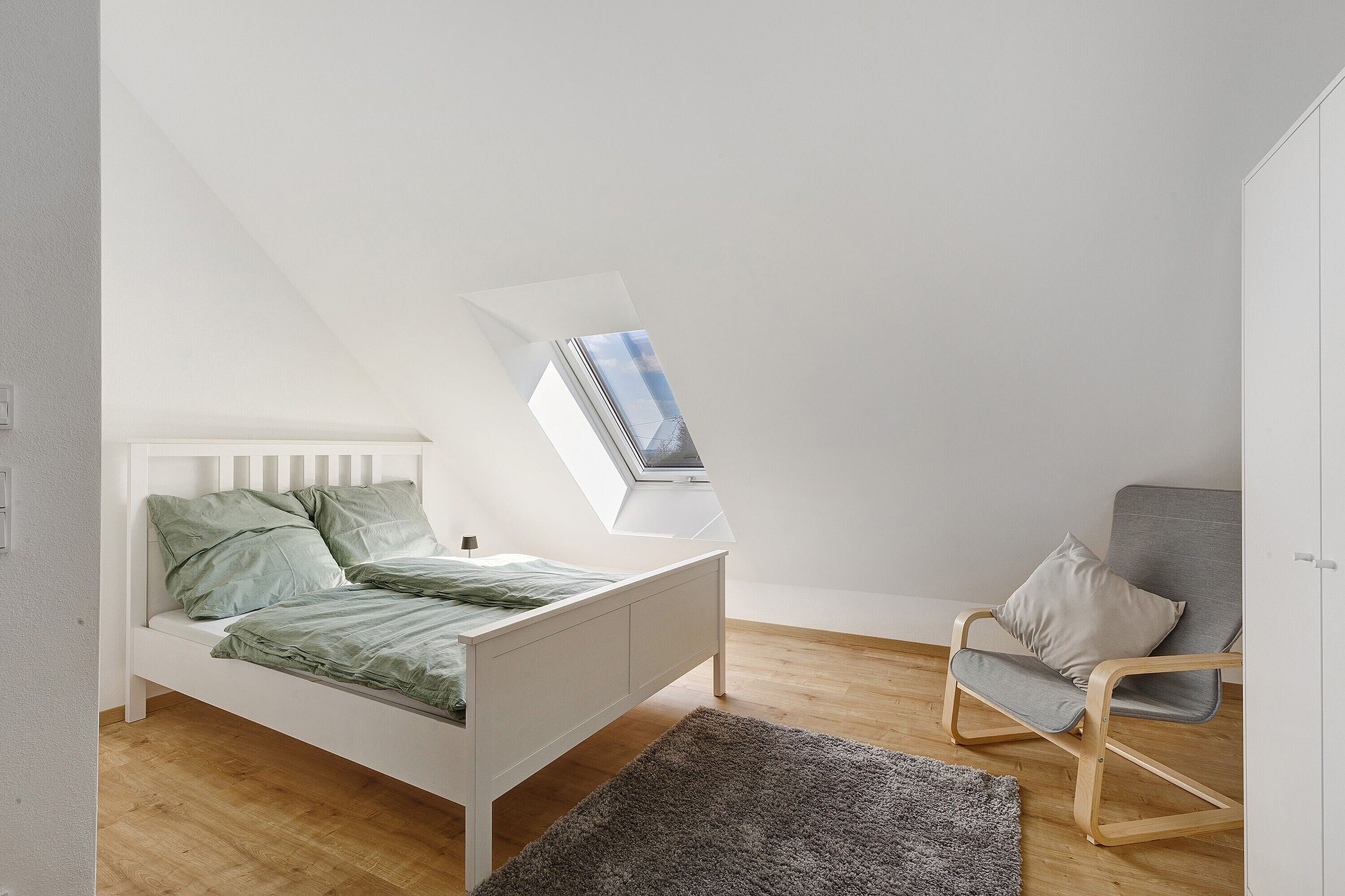 A bedroom with a bed, a chair, a skylight, and a view of the sky.