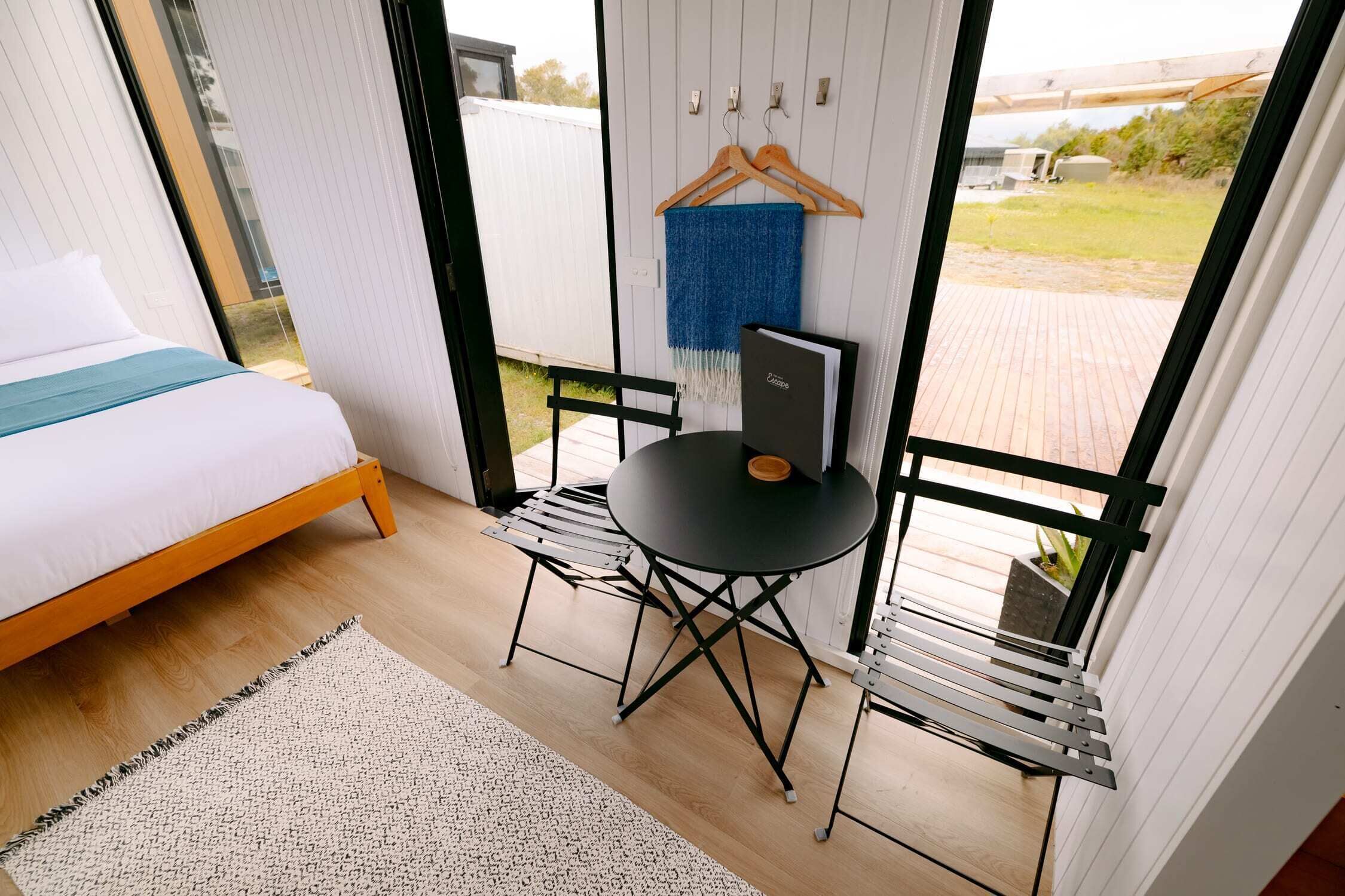 A bedroom with a bed, a small table, and a chair. There is a window with a view of the outdoors.