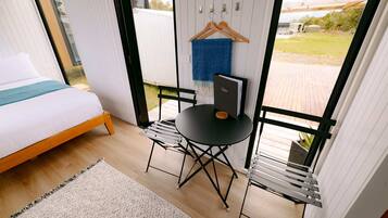 A bedroom with a bed, a small table, and a chair. There is a window with a view of the outdoors.