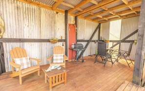 A covered outdoor area with wooden chairs, a small table, a grill, and hanging plants. - Rimu View 4 by Tiny Away (Ruatapu)