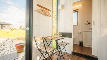 A compact room with a wooden table and chairs, a small kitchen area, and a view of the outdoors.