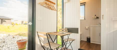 A compact room with a wooden table and chairs, a small kitchen area, and a view of the outdoors.