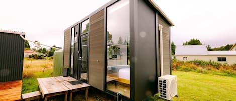 Una cabaña moderna y compacta con un amplio ventanal corredero, un pequeño patio y un equipo de aire acondicionado integrado.