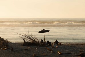 A beach scene with a tent, an umbrella, and a person sitting under the umbrella. - Rimu View 4 by Tiny Away (Ruatapu)