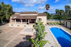 Una casa de dos pisos con piscina, rodeada de palmeras y un cielo despejado.