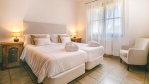 Una camera d'albergo con un letto grande, due comodini con lampade, una sedia e una finestra con tende leggere.