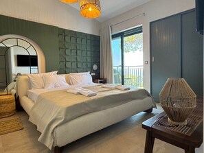 Una habitación de hotel moderna con una cama grande, un balcón con vistas y una mesa auxiliar tejida original.