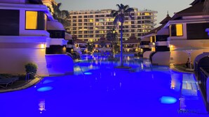 Un espace piscine d’hôtel comprenant plusieurs piscines, des palmiers et un grand bâtiment en arrière-plan.