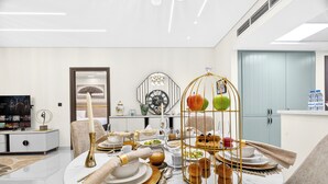 Un espace repas moderne avec une table ronde dressée pour le repas, une cage à oiseaux décorative contenant des pommes, et un téléviseur en arrière-plan.