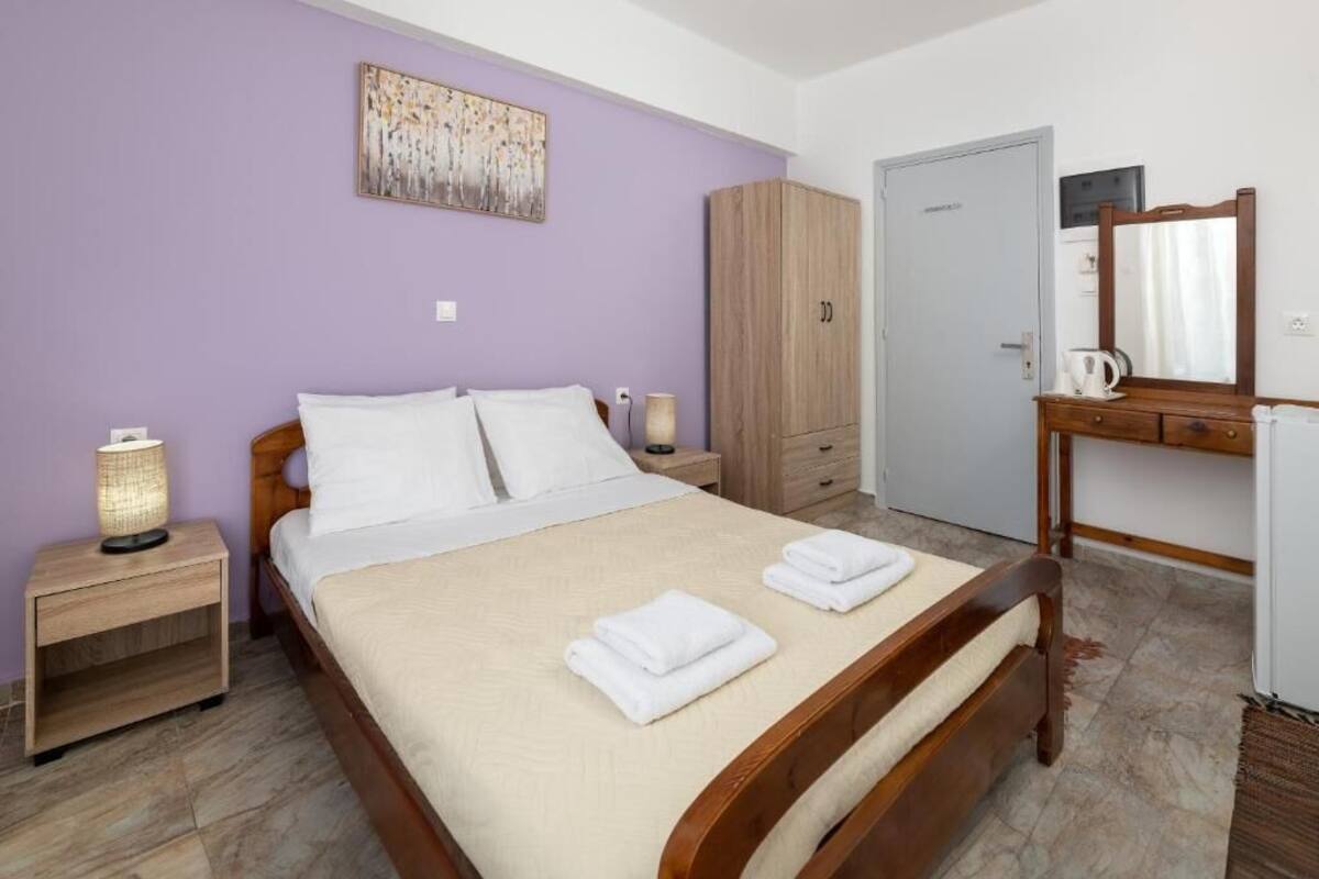 A bedroom with a bed, a nightstand, a wardrobe, a desk with a mirror, and a door.