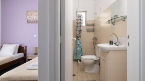 A bedroom with two beds and a bathroom with a shower, toilet, and sink. - Amethyst Rooms (Rhodes)