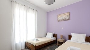 A hotel room with two beds, a wooden headboard, a nightstand, a lamp, and a painting on the wall. - Amethyst Rooms (Rhodes)