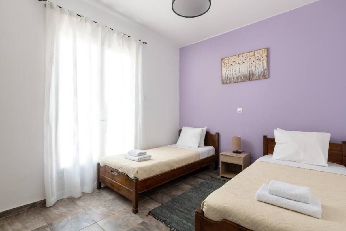 A hotel room with two beds, a wooden headboard, a nightstand, a lamp, and a painting on the wall.