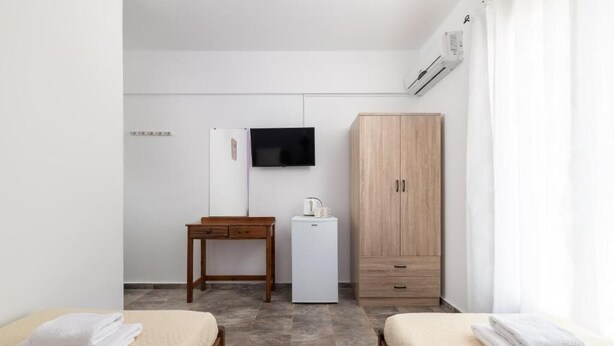 A small, modern room with two beds, a desk, a television, and a wardrobe. - Amethyst Rooms (Rhodes)