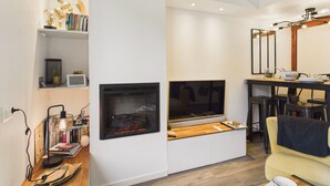 A modern living room with a fireplace, a dining area, and a sofa. - Shared pool, beach 300m, accommodation for 2 (Arzon)