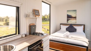 Une chambre avec un lit, une fenêtre, un petit coin cuisine avec un évier et une vue sur l’extérieur.