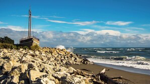 Une côte rocheuse où les vagues se brisent sur la plage, une haute structure sur la gauche et un ciel dégagé.
