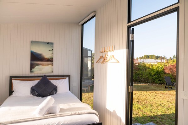 Un dormitorio con una cama, un cuadro y vistas a un jardín por una puerta corredera.