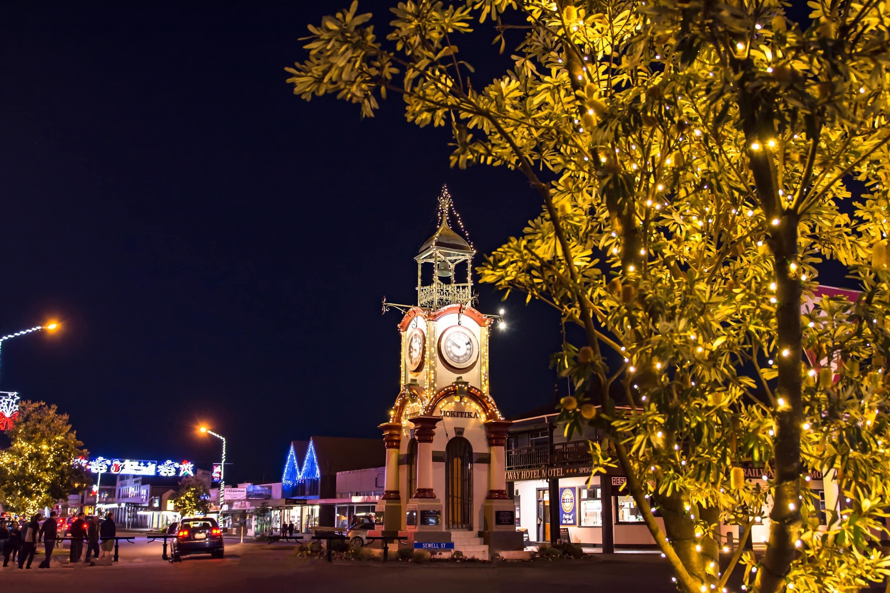 A clock tower with a clock face, surrounded by illuminated trees and buildings.