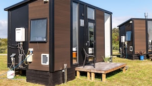 Une maison mobile moderne et compacte, dotée d’une façade en bois, de grandes fenêtres et d’un petit espace porche.