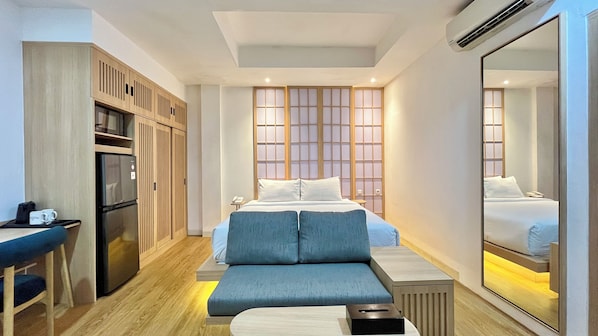 A hotel room with a bed, bedside table, seating area, kitchenette, and a large mirror. - Jambuluwuk Mansion Adityawarman (Jakarta)