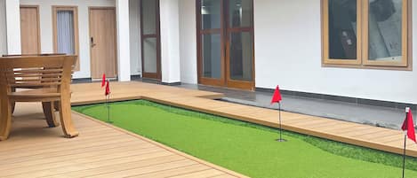 Een hotelgangen met houten vloer, een klein kunstgrasveldje en rode vlaggen die een golfbaan markeren.