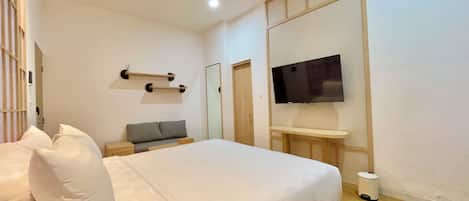A bedroom with a bed, a TV mounted on the wall, a bedside table, and a small stool.