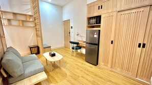 A compact living space with a sofa, a small table, a chair, a refrigerator, and wooden cabinets. - Jambuluwuk Mansion Adityawarman (Jakarta)