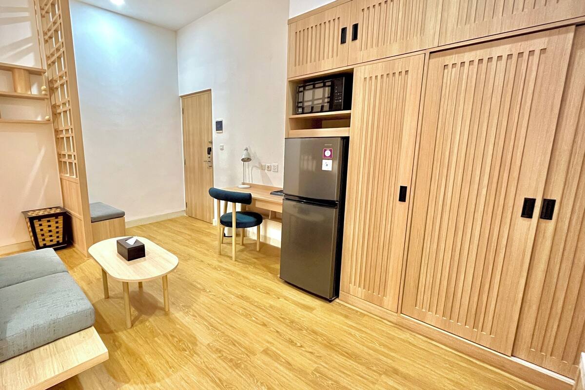 A compact living space with a sofa, a small table, a chair, a refrigerator, and wooden cabinets.