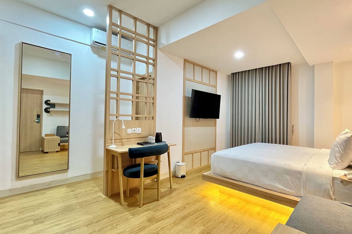 A modern hotel room with a bed, desk, chair, TV, and a large mirror.