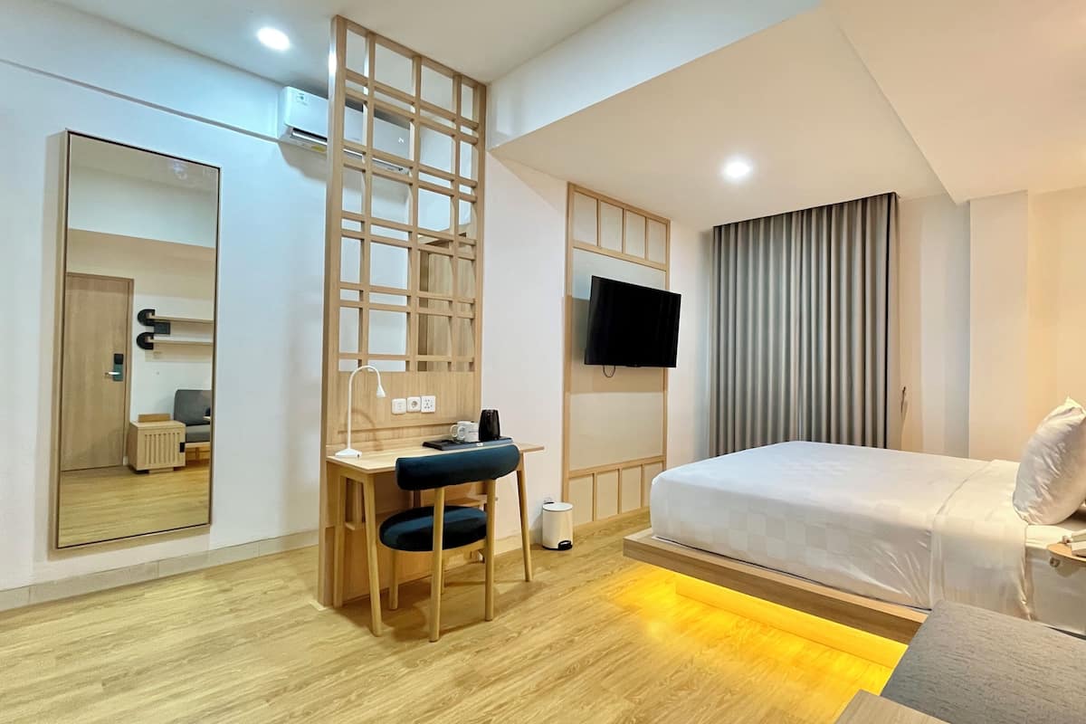 A modern hotel room with a bed, desk, chair, TV, and a large mirror.