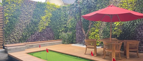 A wooden deck with a small pool, surrounded by lush greenery and a red umbrella.